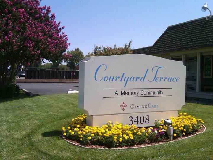 A sign for Courtyard Terrace, a memory community, surrounded by landscaping and flowers.