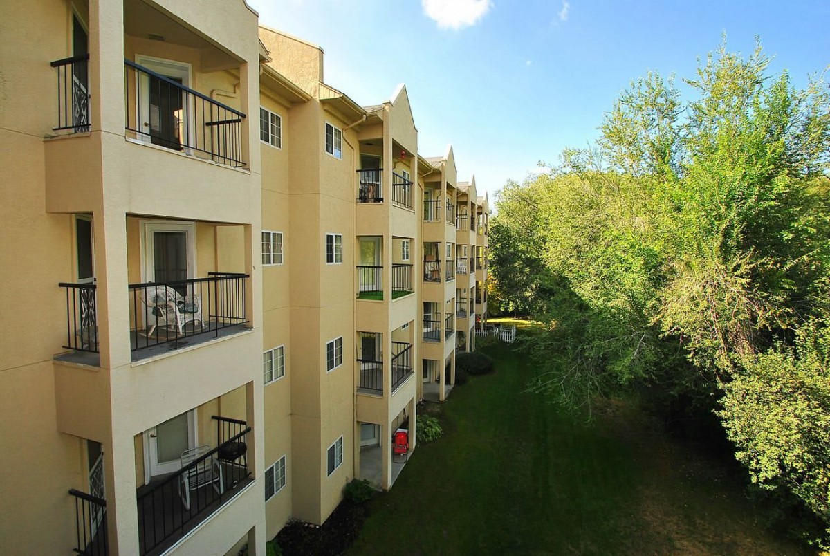 A view of a residential apartment building with multiple balconies and surrounding greenery on a sunny day.