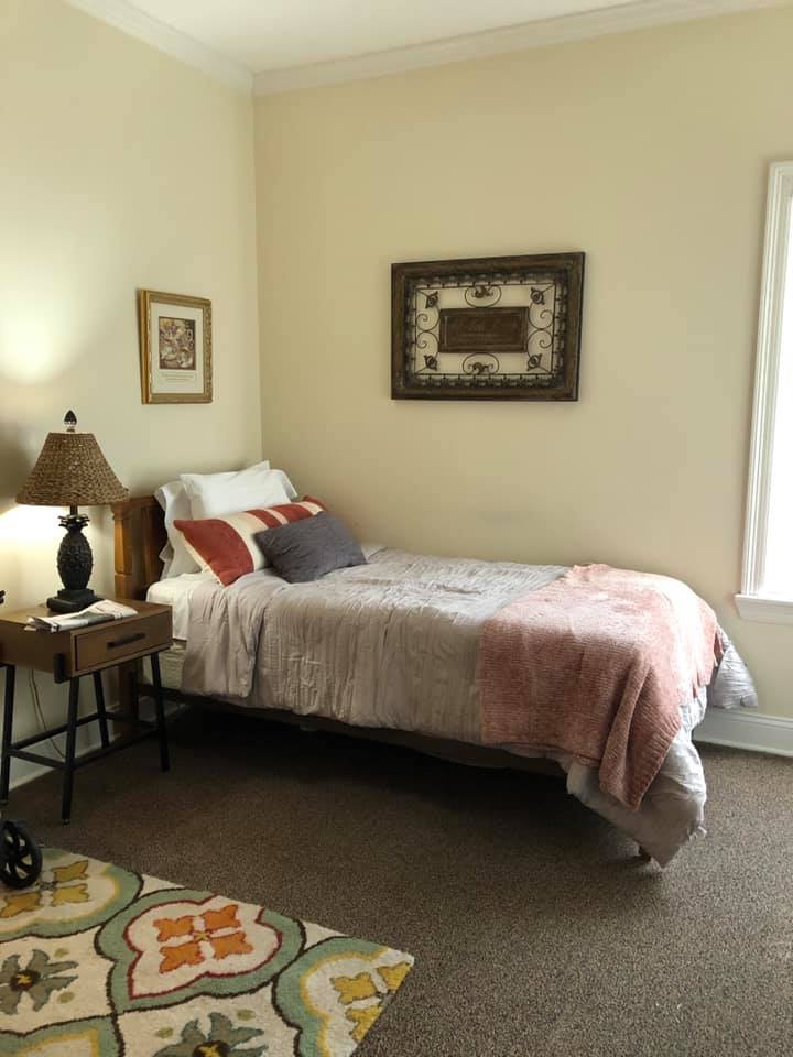 A cozy bedroom with a neatly made bed, bedside lamp, and decorative artwork on the walls.