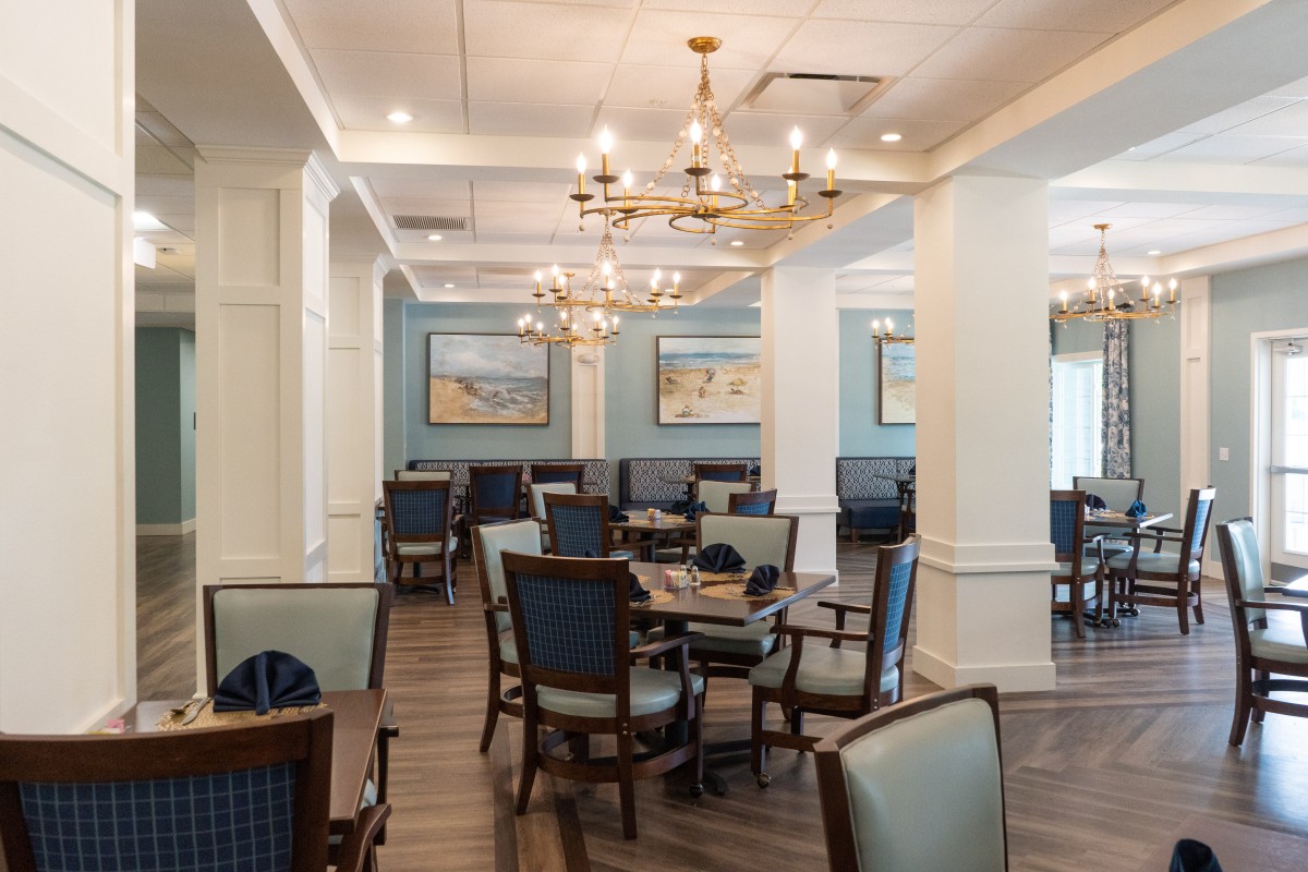 A well-lit dining area with elegant chandeliers, neatly arranged tables and chairs, and tasteful artwork on the walls.