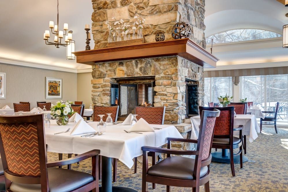 A cozy restaurant dining area featuring neatly set tables and a central stone fireplace.