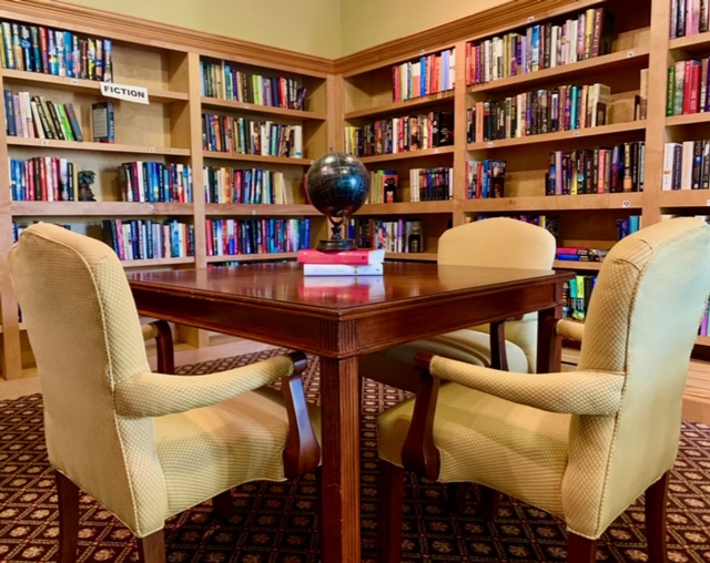 A cozy library corner with bookshelves and a wooden table surrounded by chairs.