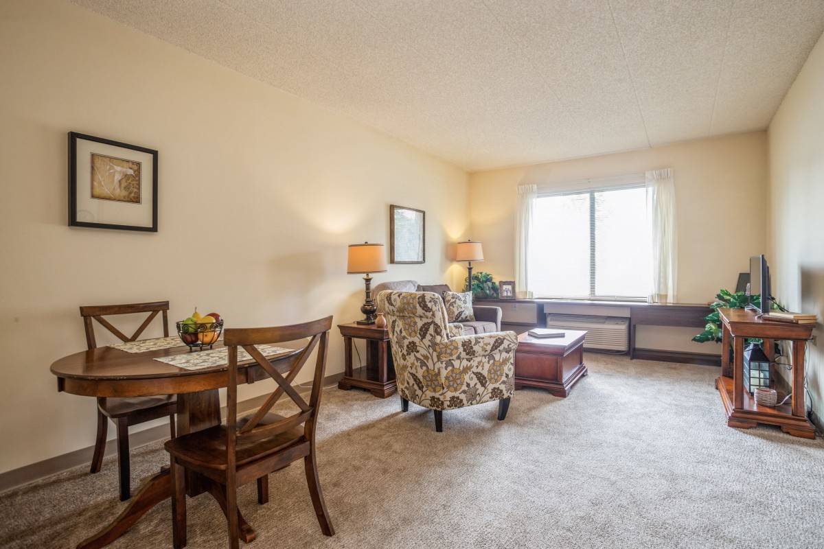 A cozy living room with a dining area, featuring comfortable seating and natural light from a large window.
