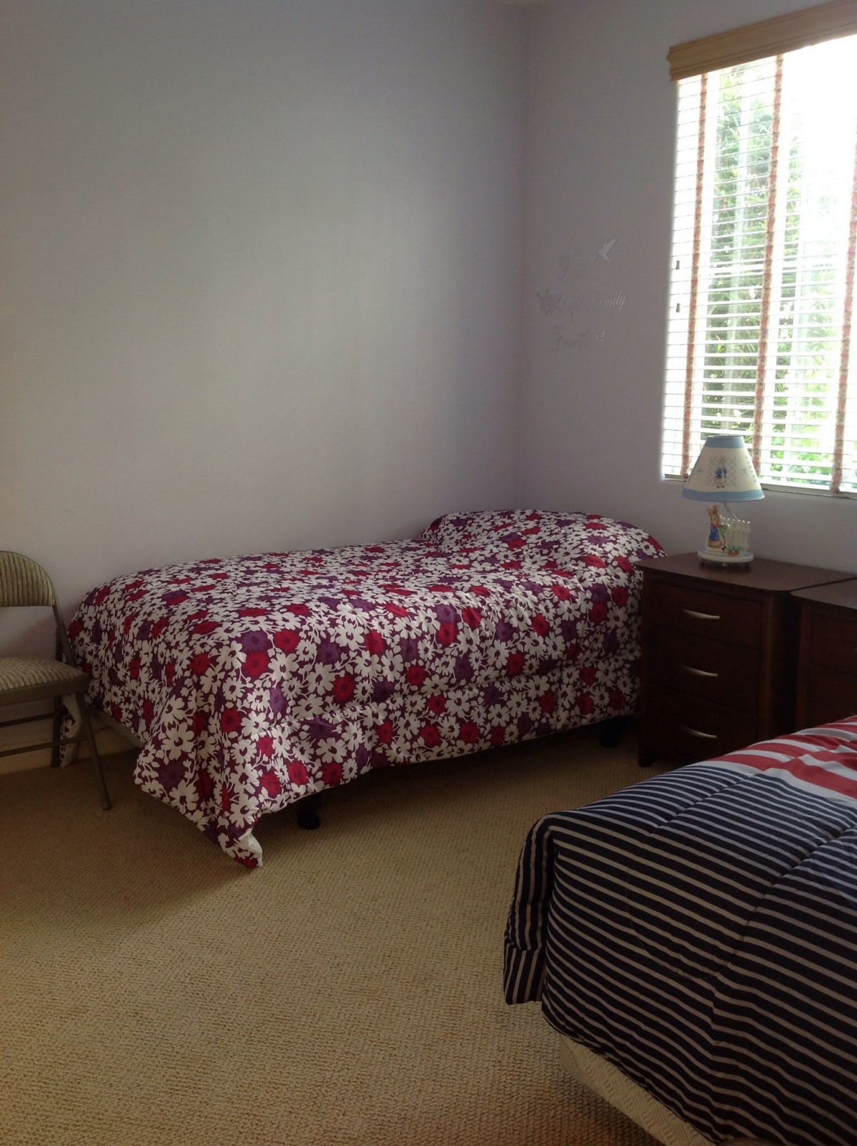 A cozy bedroom with two beds, a small lamp on a side table, and natural light filtering through the window.