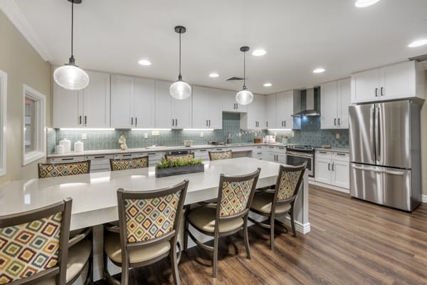A modern kitchen with a large island and stylish pendant lights, featuring white cabinets and wood flooring.
