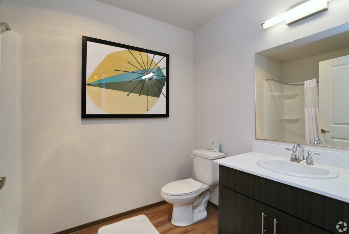 A modern bathroom featuring contemporary artwork, a toilet, and a sink with a mirror.
