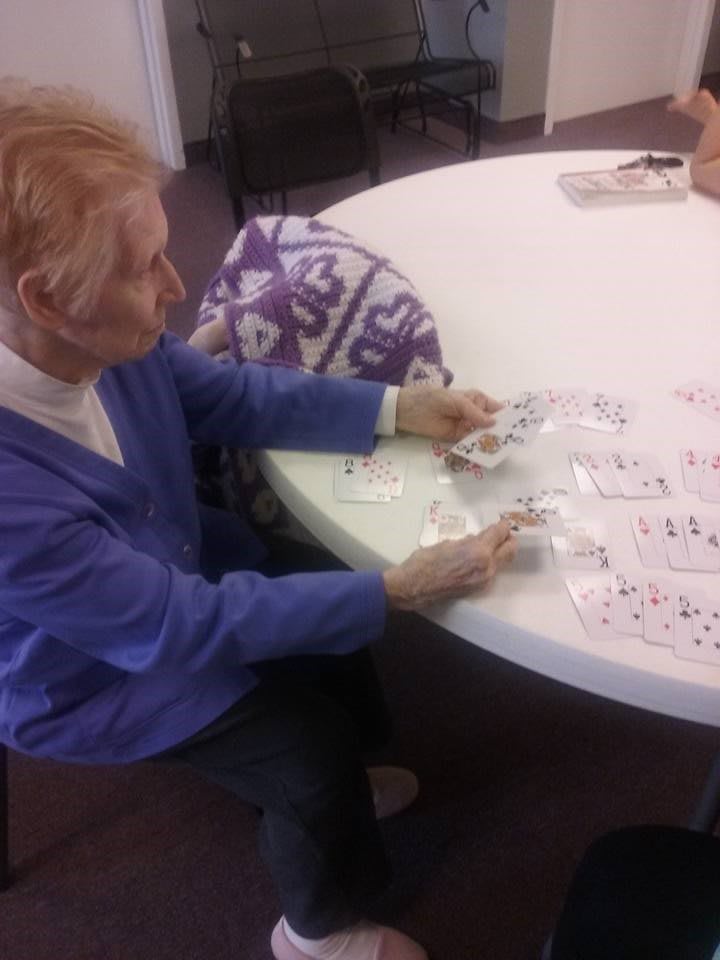 An elderly person sitting at a table playing with cards.