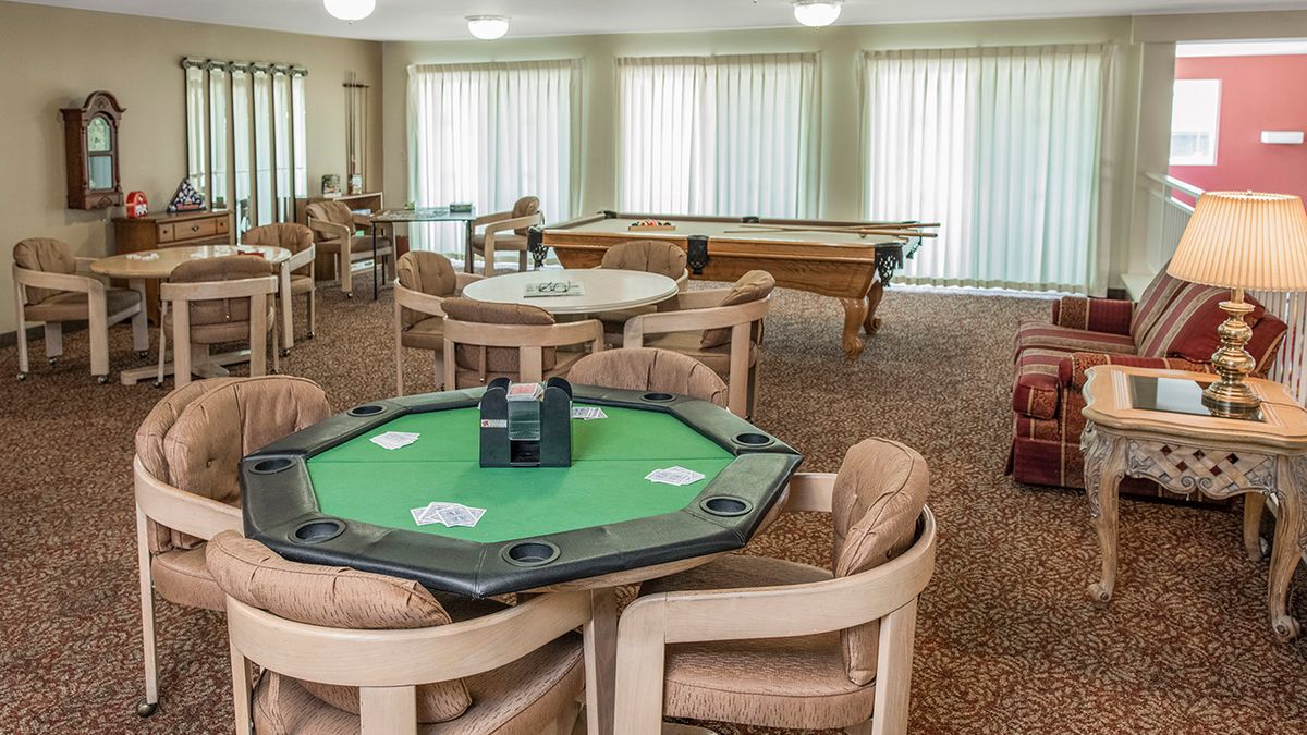 A spacious game room featuring a poker table, pool table, and various seating arrangements on a carpeted floor.