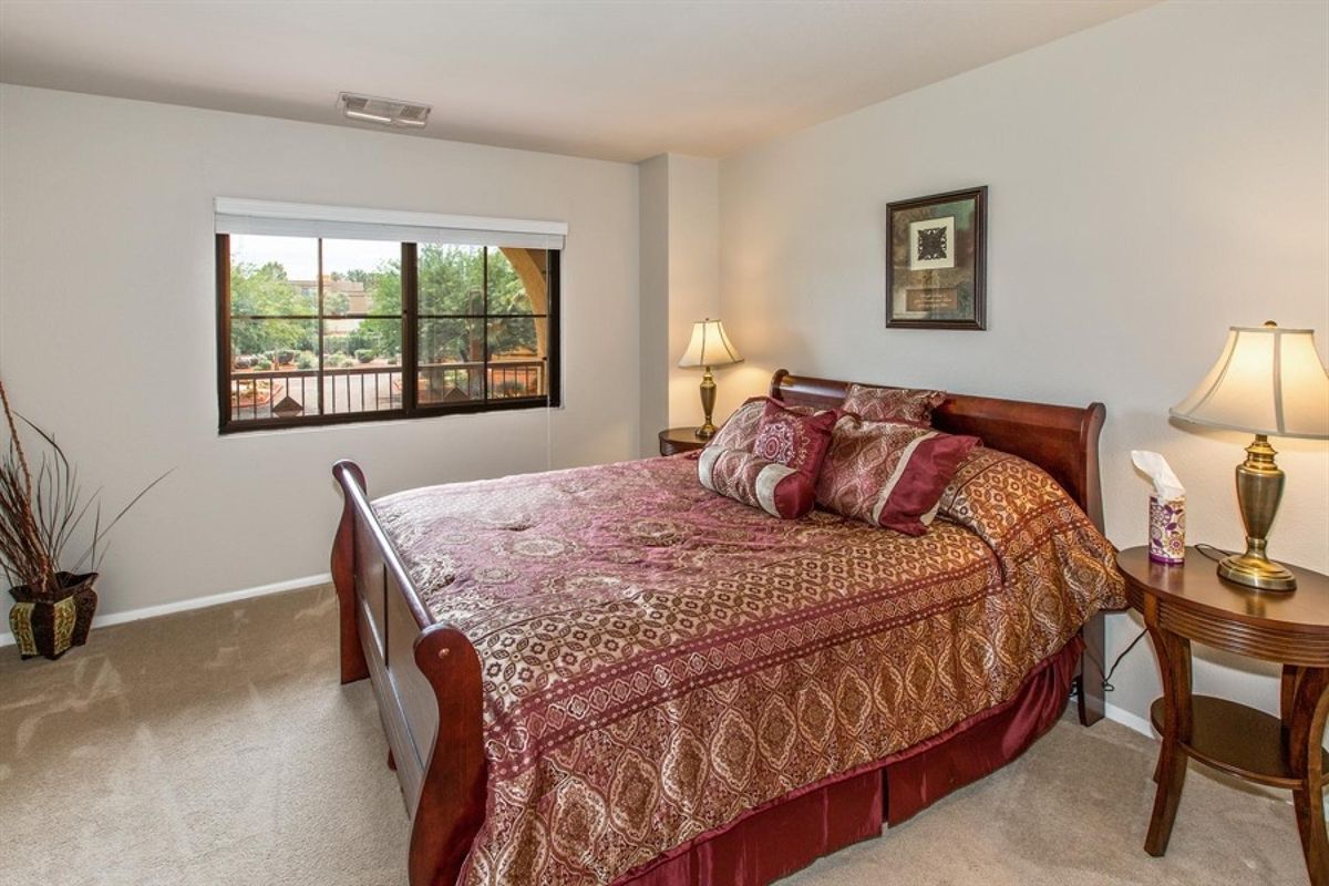 A cozy bedroom with a large bed, decorative pillows, and a bedside lamp near a window.