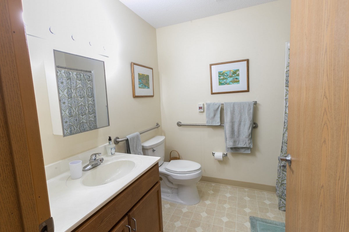 A clean and organized bathroom with a sink, toilet, towels, and framed artwork on the walls.