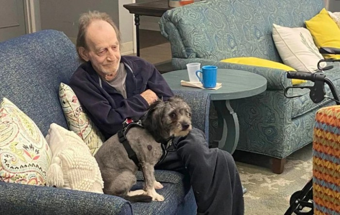 An elderly man sitting on a couch with a dog on his lap.