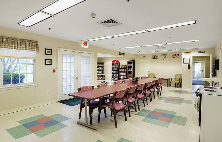 A spacious classroom with tables and chairs, featuring bookshelves and ceiling lights.