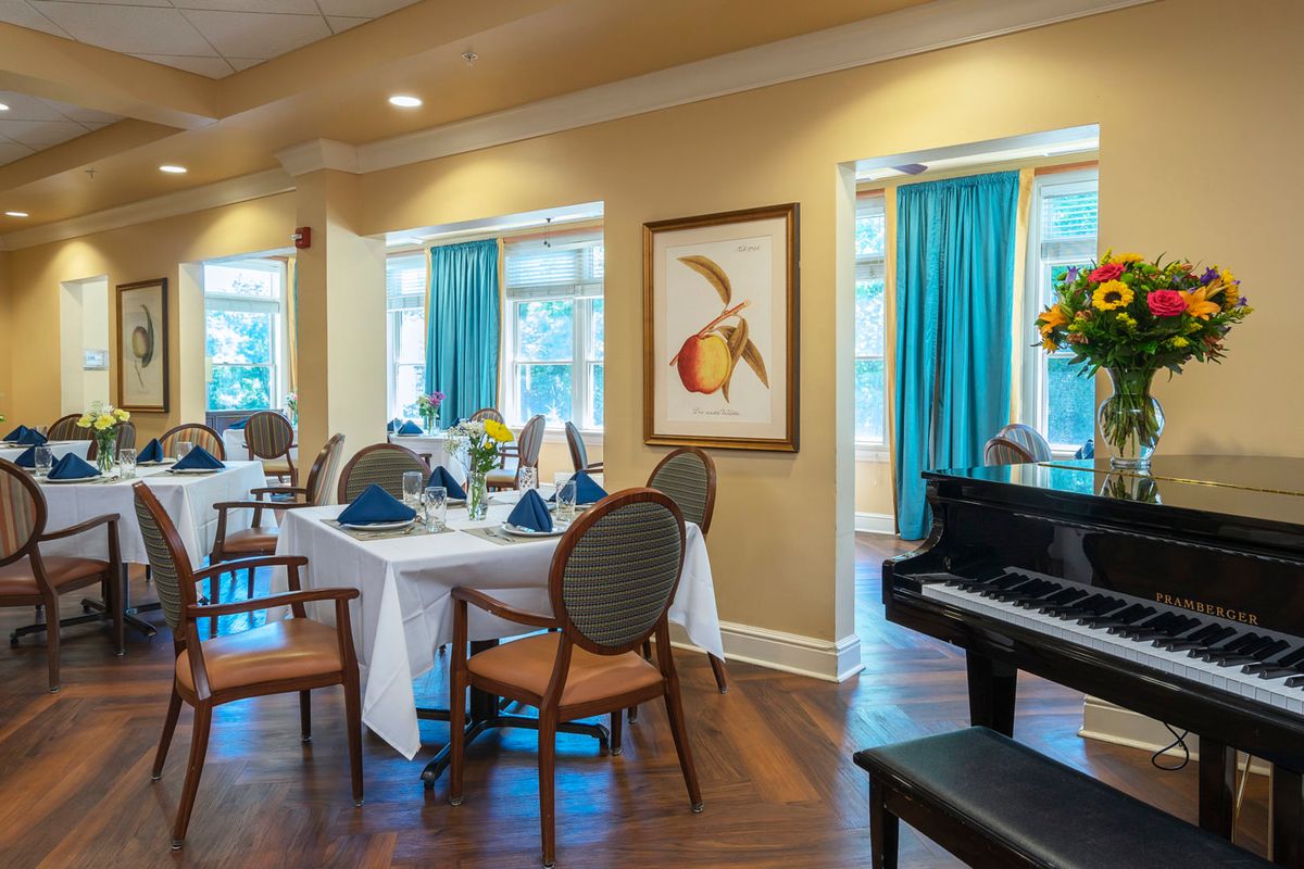An elegant dining area with set tables, a piano, and artwork on the wall.