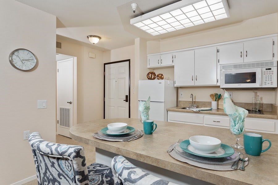 A modern kitchen in an apartment featuring white cabinets, a central countertop with place settings, and bar stools.