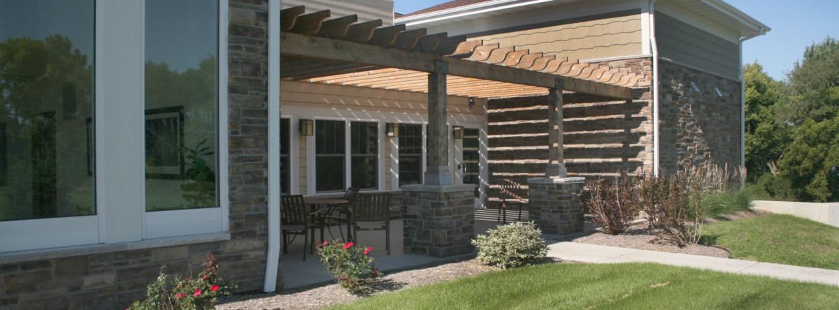 A patio with a pergola and stone columns, featuring outdoor seating and surrounding landscaping.