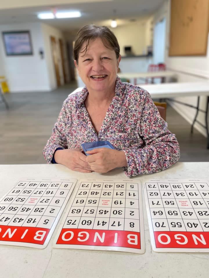 A woman sitting at a table with bingo cards in front of her, smiling at the camera.