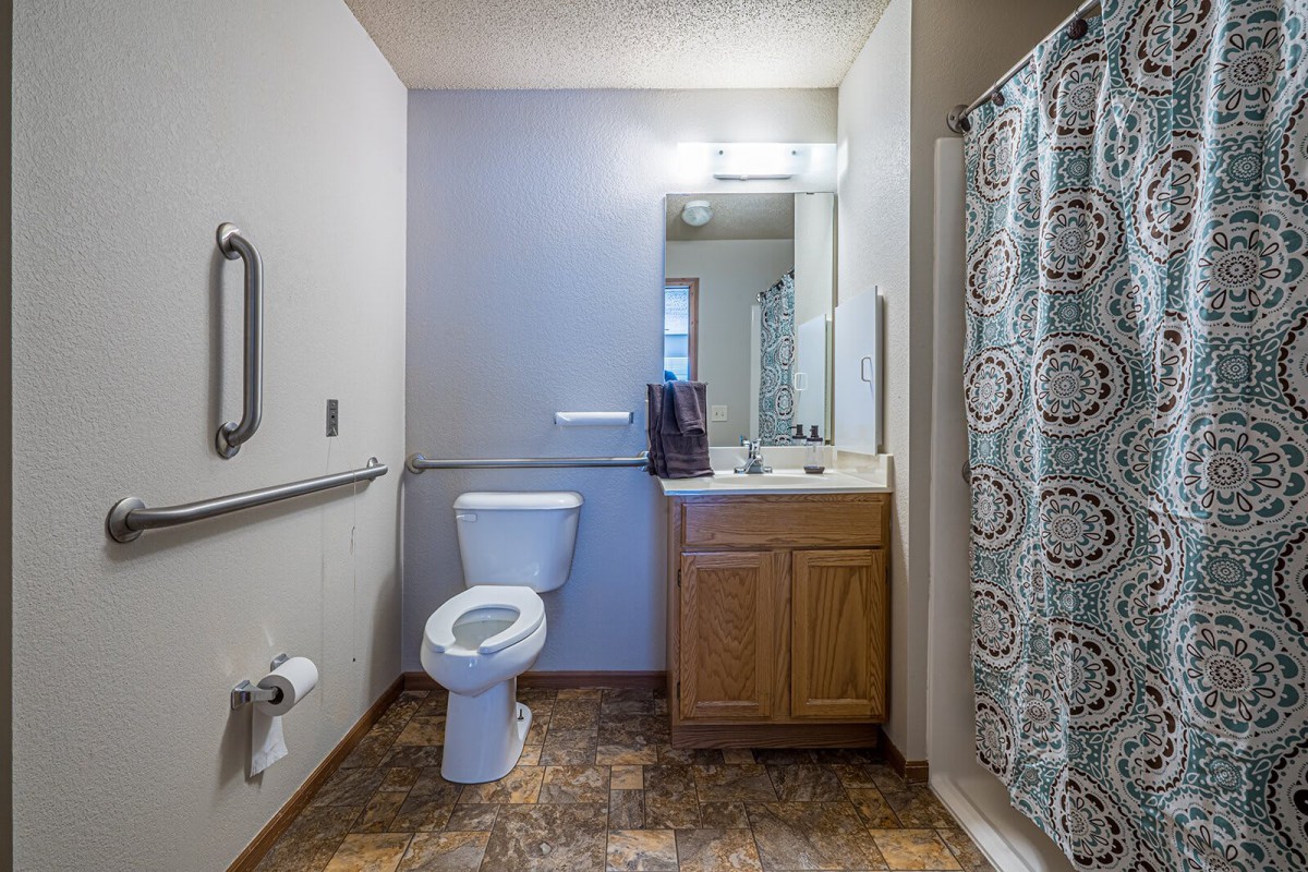 A clean and modern bathroom featuring a toilet, sink with a wooden cabinet, and a shower with a patterned curtain.