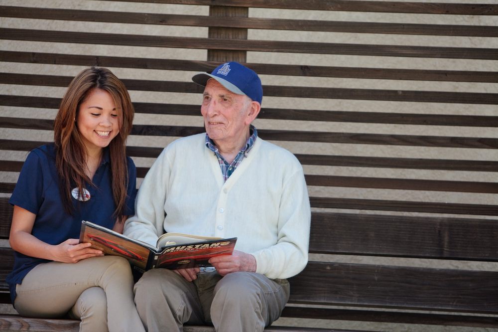 A young woman and an elderly man sitting on a bench, enjoying a book together.