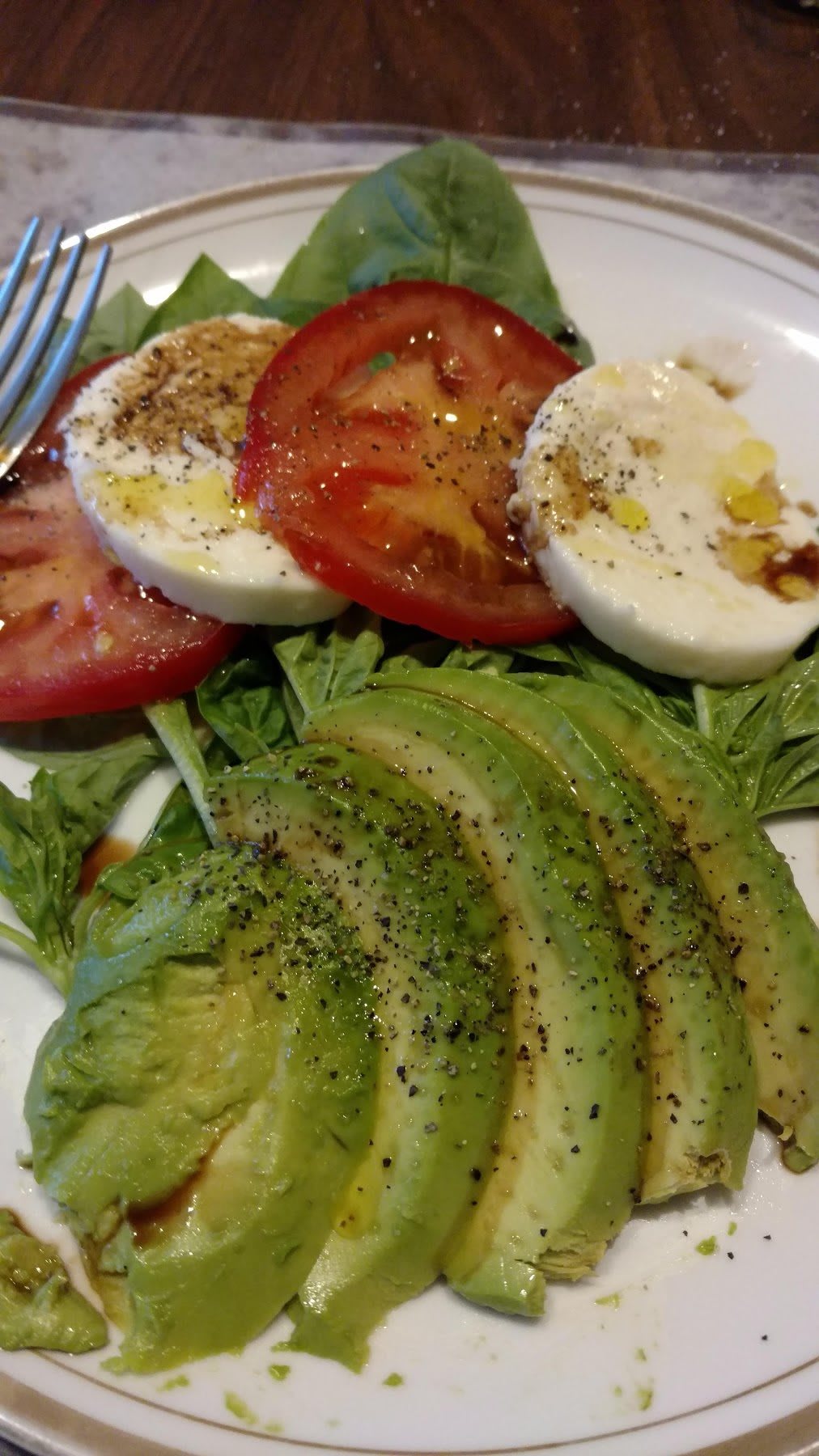 A fresh salad featuring slices of avocado, tomato, and mozzarella with a drizzle of olive oil and herbs.