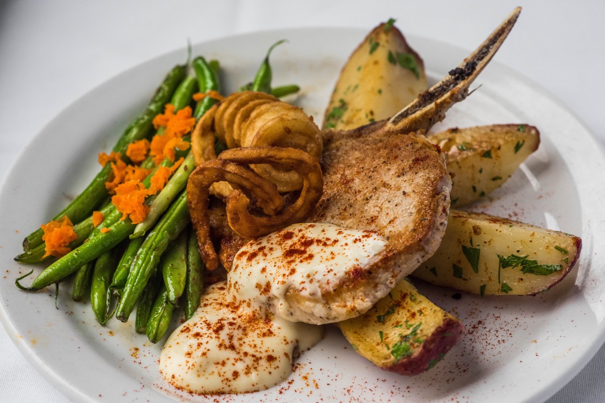 A savory pork chop with creamy sauce served alongside crispy onion rings, tender green beans, carrots, and potatoes.