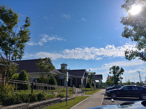 A clear day with a blue sky and puffy clouds over a well-maintained building and parking area.