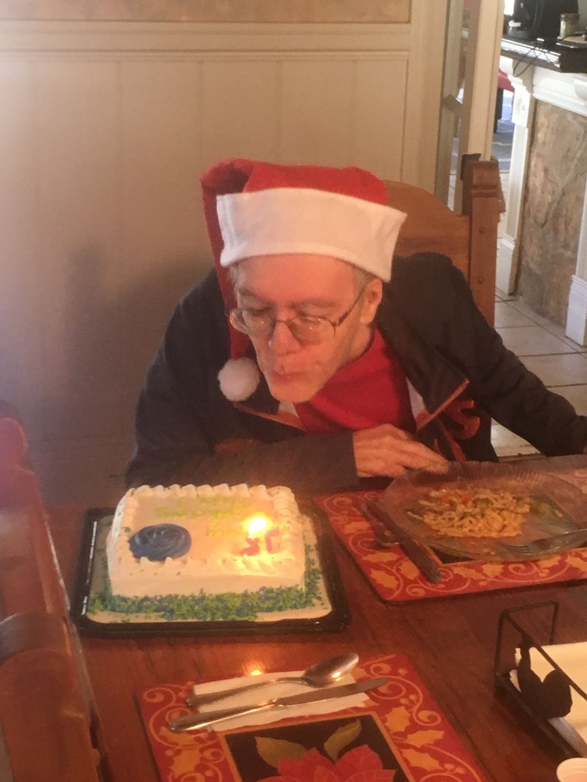 A person wearing a Santa hat blows out candles on a birthday cake.