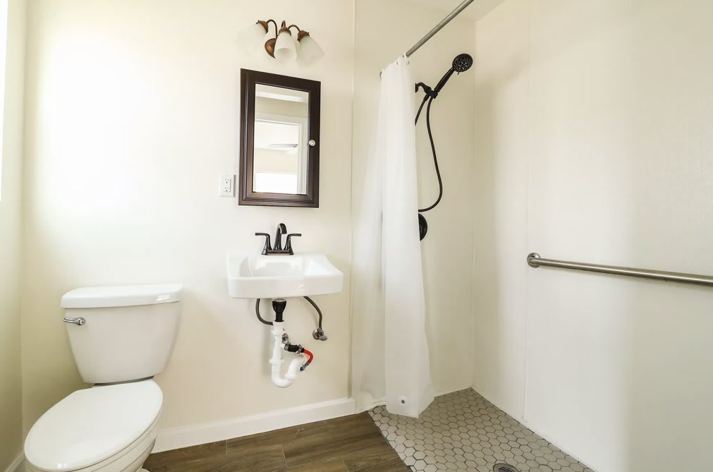 A modern bathroom with a wall-mounted sink, mirror, and walk-in shower featuring black fixtures.