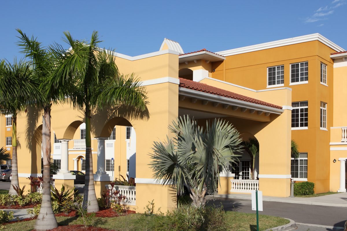 A sunny view of a hotel building with palm trees and landscaped gardens.