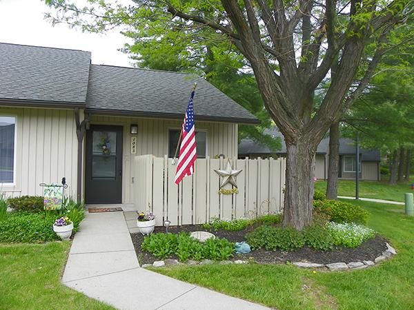 A small house with an American flag and a garden, shaded by a large tree.