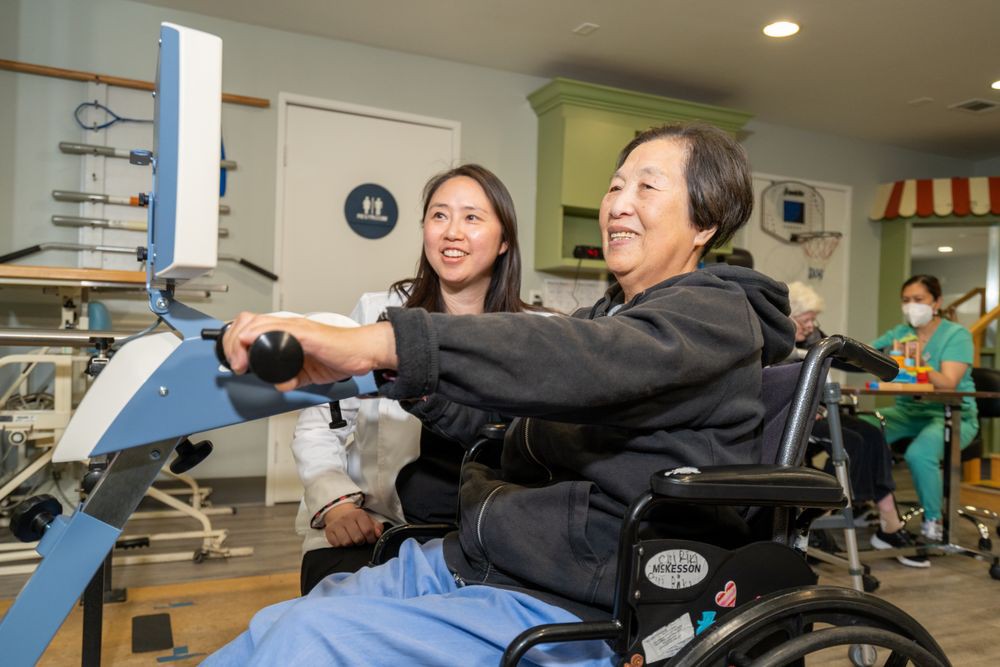 An elderly person in a wheelchair participating in a therapy session with assistance.