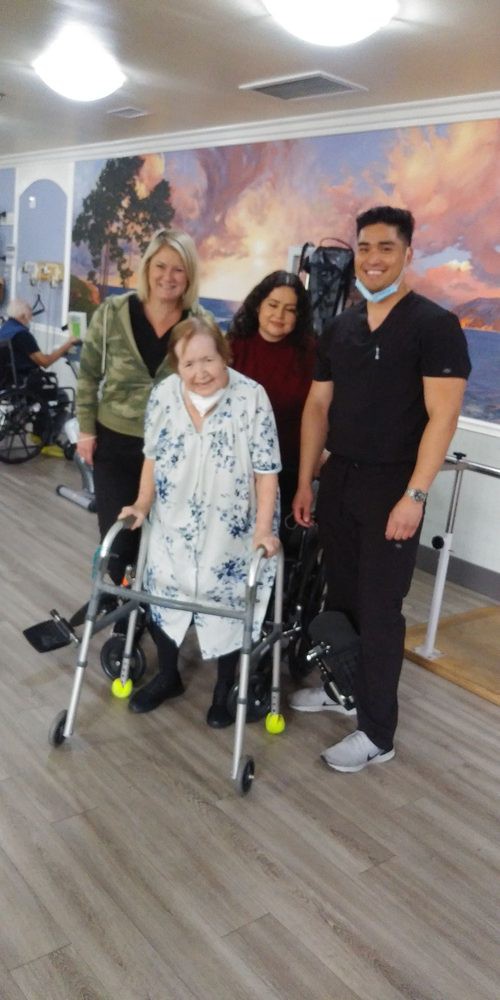 A group of people, including an elderly woman using a walker, pose for a photo indoors.