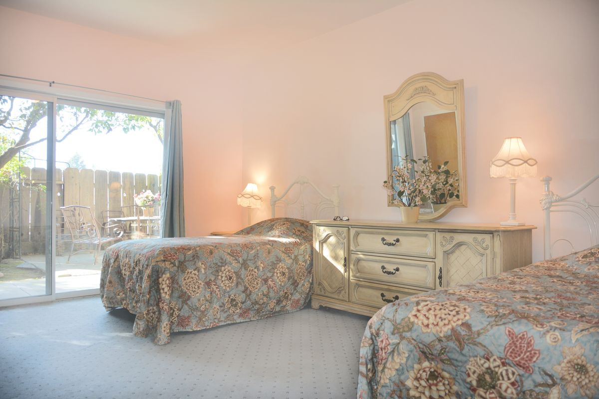 A cozy bedroom with twin beds featuring vintage furniture and floral bedding, illuminated by natural light.