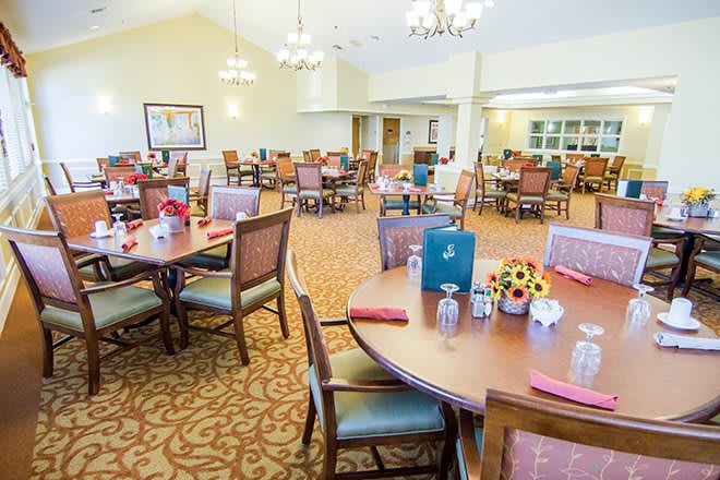 A spacious dining room with neatly arranged tables and chairs, featuring elegant chandeliers and warm decor.