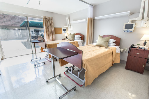 A spacious and well-lit patient room in a modern hospital, featuring two neatly made beds and functional furniture.
