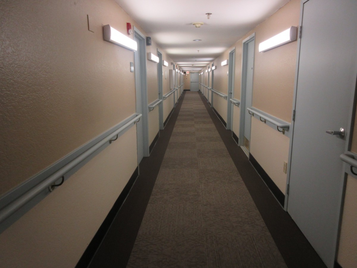 A long, empty hallway with doors on either side and fluorescent lighting overhead.