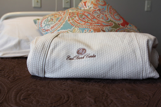 A neatly rolled towel featuring embroidered branding, resting on a stylish bed with patterned pillows.