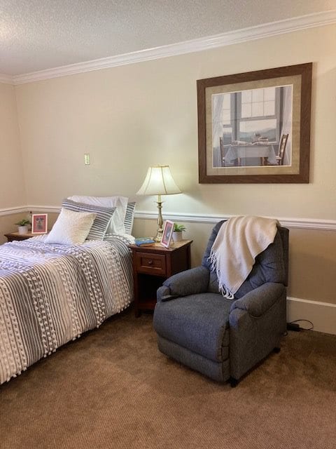 A cozy bedroom with a neatly made bed, a comfortable armchair, and a bedside lamp.