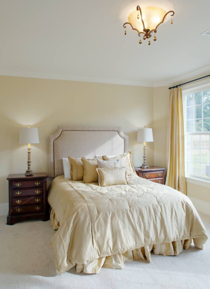 A cozy bedroom with a neatly made bed, flanked by two nightstands and lamps, illuminated by natural light from a large window.