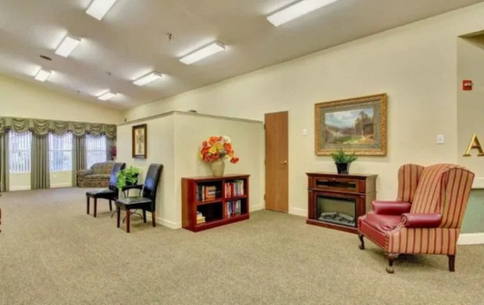 A cozy waiting room with comfortable chairs, a bookshelf, and decorative elements, including a painting and plants.