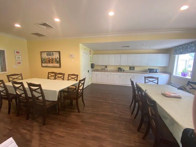 A spacious dining room with multiple tables and chairs, adjacent to a kitchen area.
