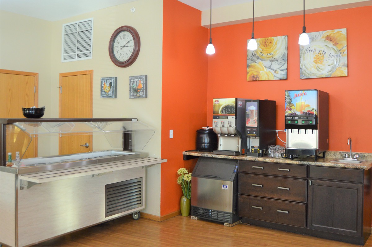 A cozy kitchen area featuring a coffee machine, orange accent wall, and stylish pendant lighting.