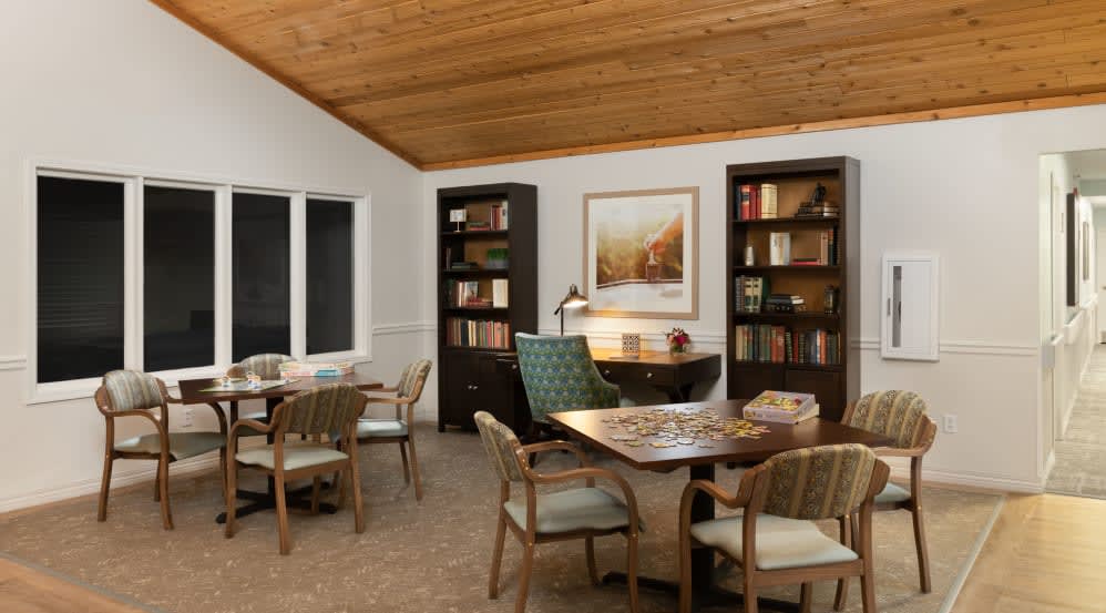 A cozy library room with wooden bookshelves, tables, and chairs under a wooden ceiling.