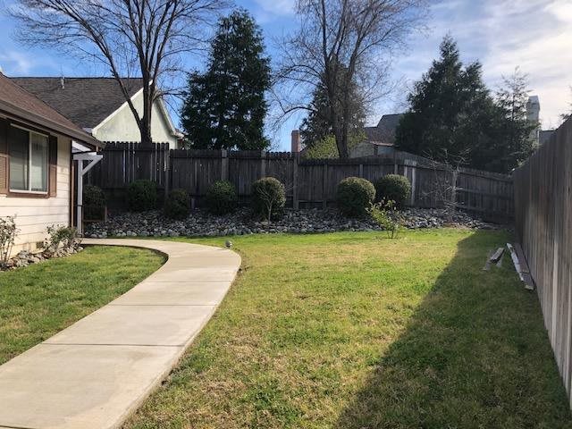 A serene backyard featuring a curved pathway, grass, trees, and a wooden fence.