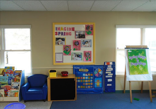A cozy preschool classroom featuring a colorful spring-themed bulletin board and comfortable seating for young learners.