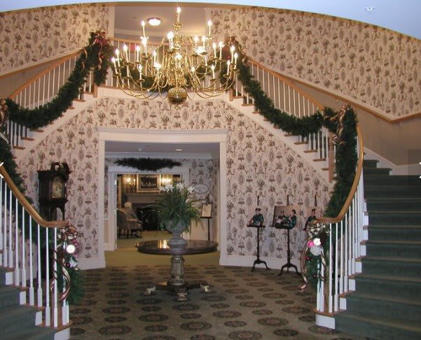A beautifully decorated grand staircase adorned with Christmas garlands and a chandelier, exuding traditional holiday charm.