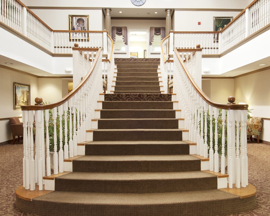 A grand, carpeted staircase with wooden railings leading to the upper floor of a luxurious interior.