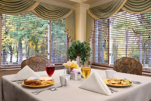 A beautifully set dining table with plates and drinks by large windows adorned with elegant curtains.