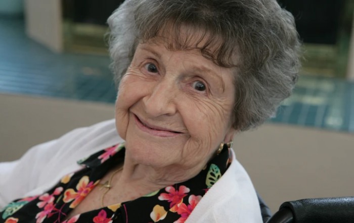 An elderly woman smiling warmly indoors.