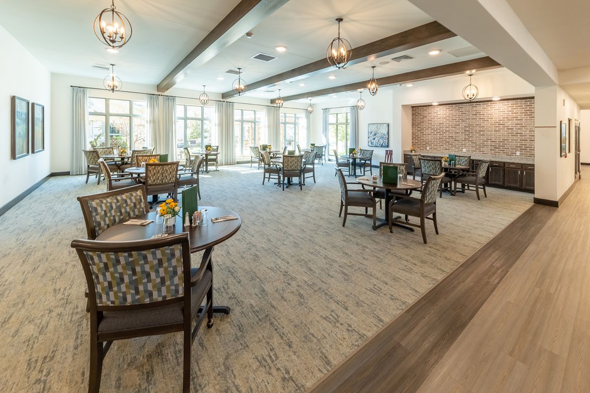 A spacious and elegantly designed dining area with multiple tables and chairs, featuring modern lighting fixtures and large windows.