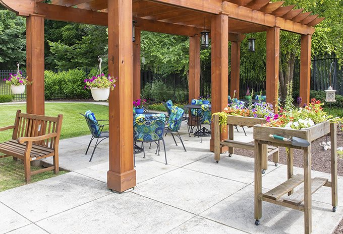 A beautifully set patio with a wooden pergola and colorful chairs overlooking a lush garden.